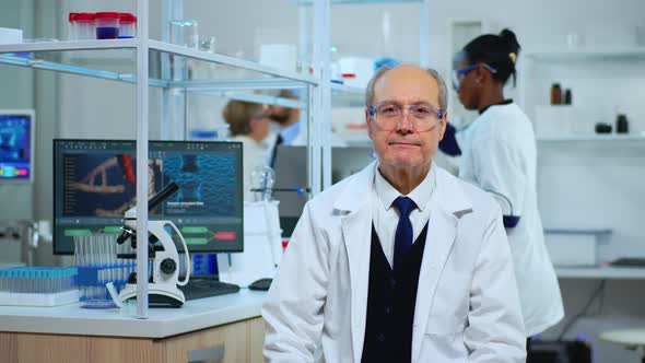 Senior Biochemist Sitting in Lab Looking Satisfied at Camera