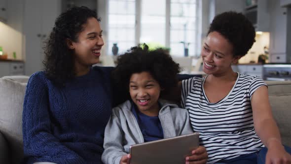 Smiling mixed race lesbian couple and daughter using digital tablet on couch