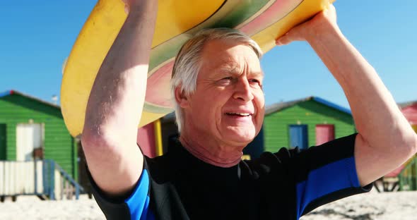 Senior man in wetsuit carrying surfboard over head