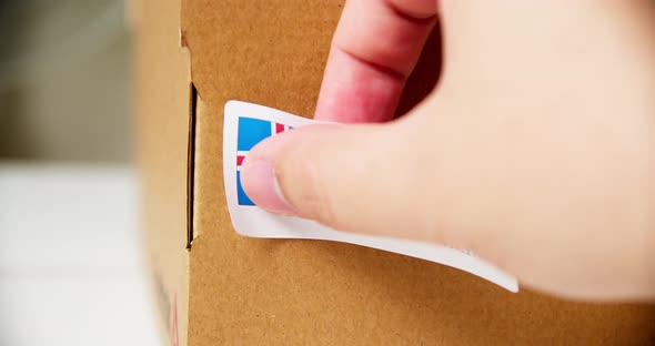 Hands applying MADE IN ICELAND flag label on a shipping cardboard box with products. Close up shot w