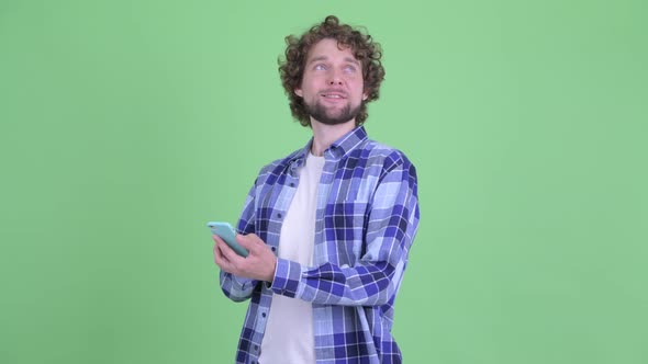 Happy Young Bearded Hipster Man Thinking While Using Phone