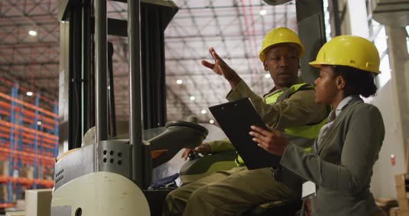 African american male and female workers wearing safety suits and talking in warehouse