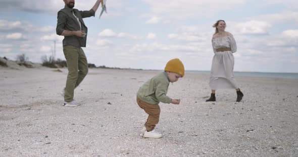 Little boy child playing with kite. European family parents playing together on the beach at summer alt