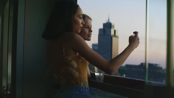 Girls taking pictures out of balcony with smartphone and smiling