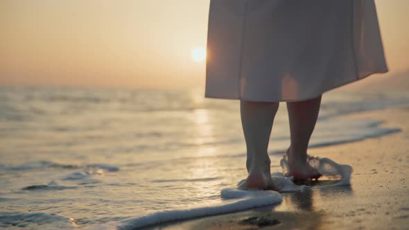 Young woman in a summer dress walking on the waves on the seashore