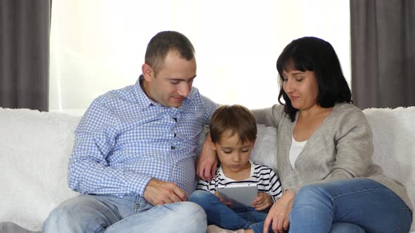 Happy Family: Father, Mother and Son Use Tablet While Sitting on Sofa. Parents and Child Have Fun