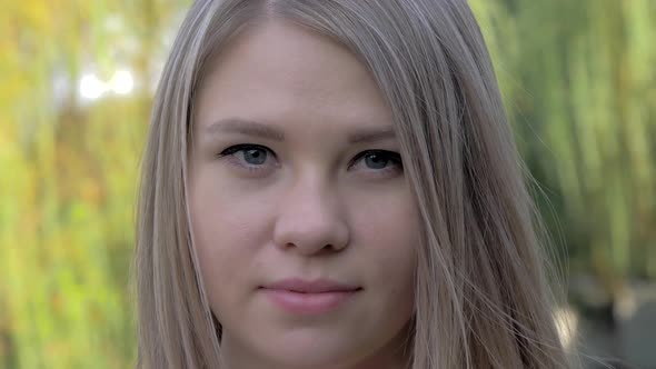 Portrait of a Beautiful Blonde Girl with Waving Hair Looking at Camera in the Park on Sunny Day