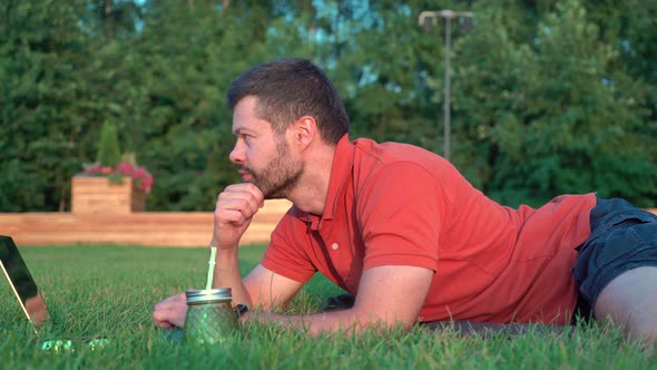 Man lying on grass and working on laptop