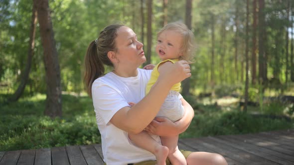 Little Cute Baby Toddler Girl Blonde with Curls on Mother's Arms