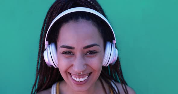 Mixed race girl listening music playlist outdoor with green background while smiling on camera