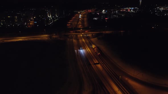 Retreating night aerial tilts up to reveal light winter city traffic