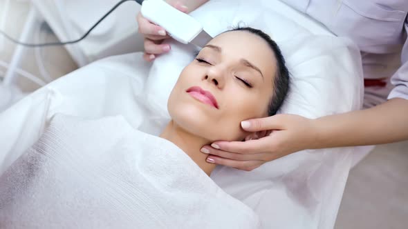 Medium Closeup Hands of Cosmetologist Making Beauty Facial Procedure Using Modern Peeler Equipment