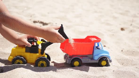 Close-up of a Boy's Tanned Hands Playing on the Beach with Cars, a Plastic Toy Car, an Excavator