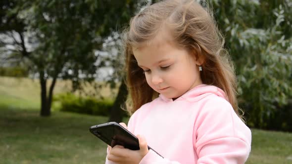 Little Caucasian Girl is Using Her Mobile Phone for Texting and Watching Videos or Playing Games