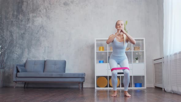 Young and sporty girl in sportswear is using resistance band while doing at home.