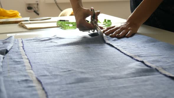 Female Seamstress Hands with Manicure Cut Off Blue Colored Fabric with Special Sewing Scissors