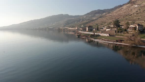 Aerial of train driving next to lake and a beautiful small town in Swiss countryside