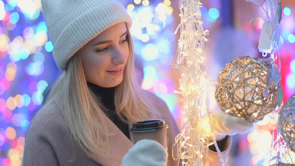 happy girl in warm clothes with a cup of hot coffee chooses decorations at the Christmas fair.