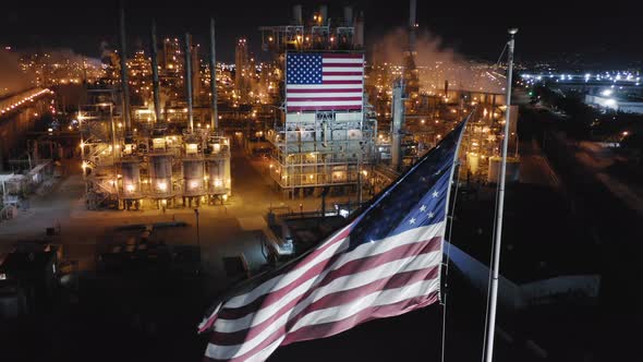 Waving Flag of United States Against the Background of Petroleum Refinery at Night