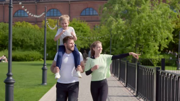 Slider Shot of Little Boy on Father Shoulders Having Fun with Parents Outdoors