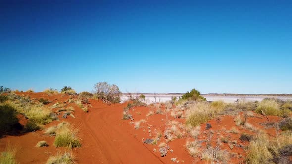 Drone reveals huge dry salt lake after flying up over remote red dirt trail in Australian outback.