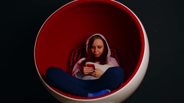 Woman Browsing Smartphone in Egg Armchair