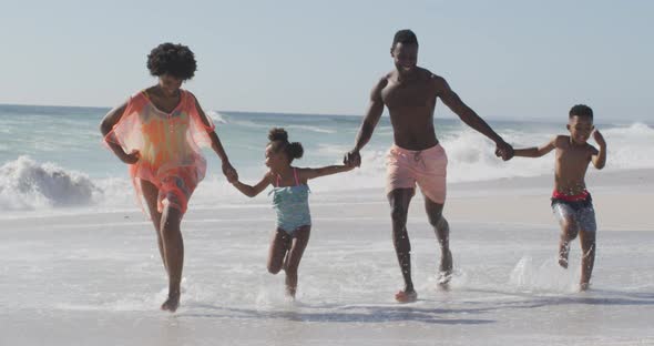 Smiling african american family holding hands and running on sunny beach