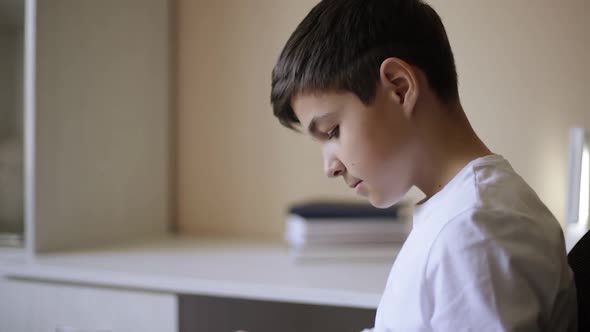 Young Boy Sitting By the Desk and Read the Book. Study at Home During Quarantine. Distance Learning