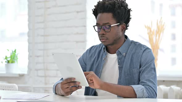 Young African Man Scrolling on Tablet in Office