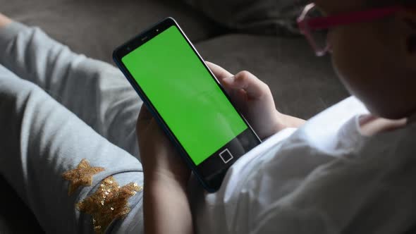 A Happy Little Girl Looks at the Green Screen of Her Mobile Phone and Laughs at a Funny Movie