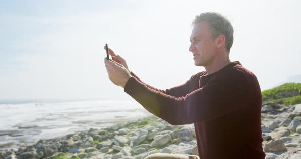 Caucasian man enjoying free time by sea on sunny day sitting on smartphone