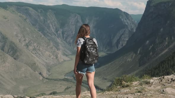 A Female Traveler with a Rucksack Climbs To the Top of the Mountain and Raises His Hands Up Feeling