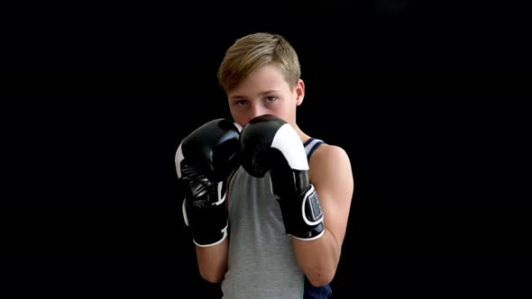 A Teenage Boxer Is Doing Sports with Gloves and a Gray T-shirt on a Dark Background. The Boy Has