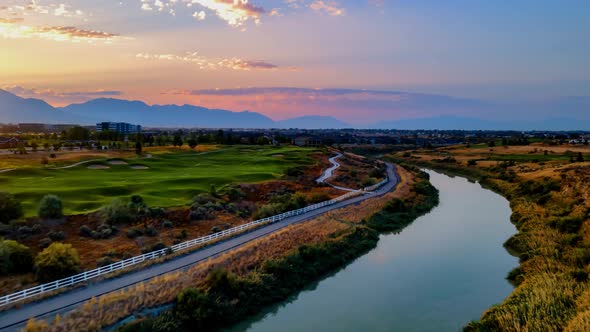 Aerial hyperlapse over a river with the rising sun and an idyllic community with a golf course, comm