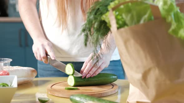 woman in the kitchen on the table cuts ripe cucumbers for a vegetable salad