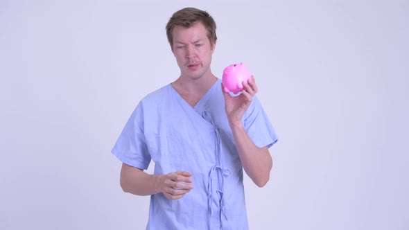 Stressed Young Man Patient Holding Piggy Bank and Giving Thumbs Down