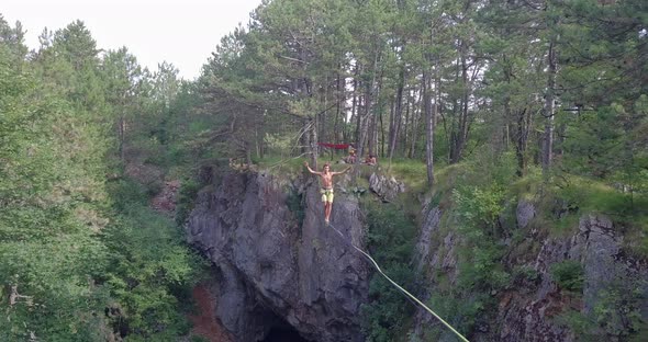 A man tries to balance while slacklining on a tightrope in the mountains.