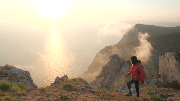 Young Man Walks Along the Edge of a Cliff Observing Beautiful Dramatic Colorful Sunset Above a Sea