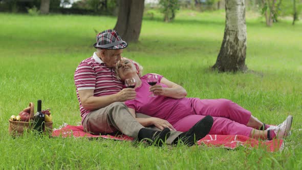 Family Weekend Picnic in Park. Senior Old Couple Sit on Blanket and Drink Wine. Making a Kiss. Love