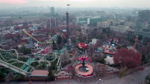 Aerial orbit of amusement park rollercoasters, rides and extreme games, Santiago city buildings in b