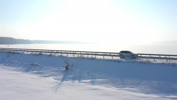 Aerial Shot of White Car Riding Through Snow Covered Road Near a Frozen Lake