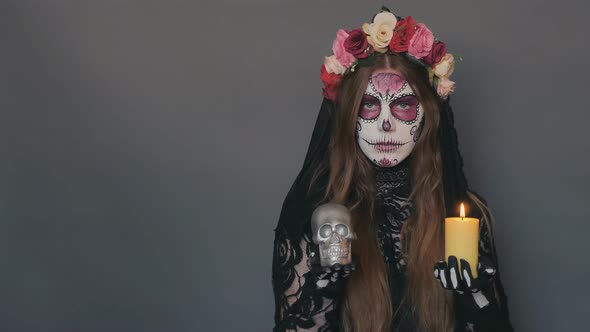 Woman in the Image of Death Santa Muerte or Sugar Mexican Skull with a Burning Candle and a Skull in