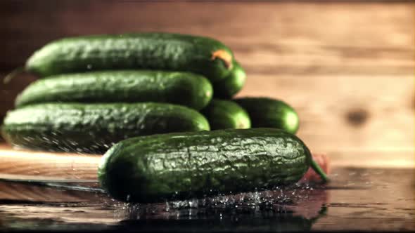 A Fresh Cucumber Falls on the Table with Splashes of Water