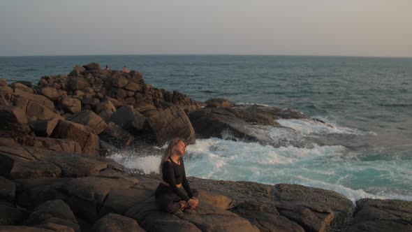 Young Woman in Black Tracksuit Stretches on Grey Rocky Cliff