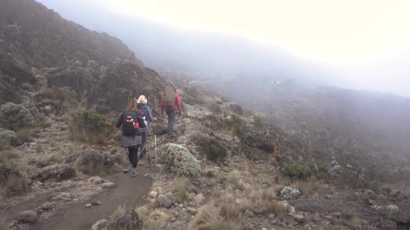 Pan Shot of Two Hikers and a Guide on Mount Kilimanjaro Walking trough Misty Clouds with other Hiker