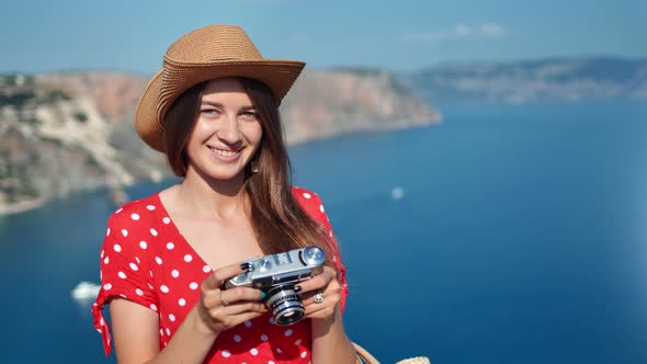 Beautiful Travel Woman in Hat Posing Holding Camera at Sea Landscape Background at Sunny Summer Day