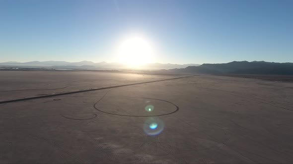 Flying over the Bonneville Salt Flats in Utah by drone, a causeway and car tracks are visible at sun