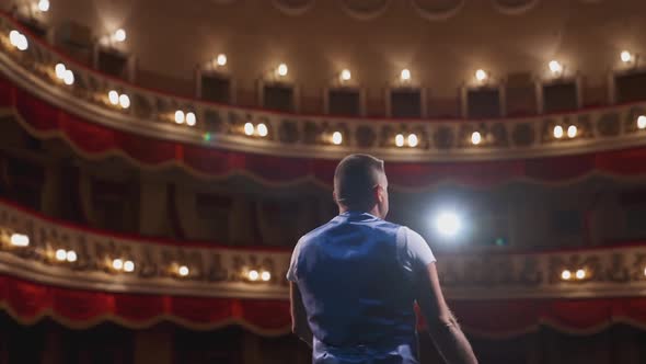 Actor on theater scene with his back to the camera. Man on stage bowing and actively gestures