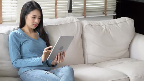 Young asian woman using tablet computer with smile and happy sitting on couch at living room.