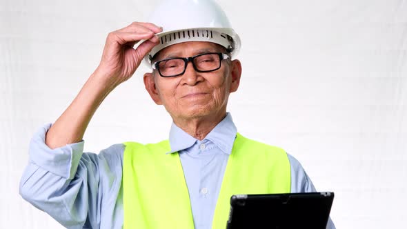 Senior architect of construction engineering wearing a vest and helmet holds a digital tablet.